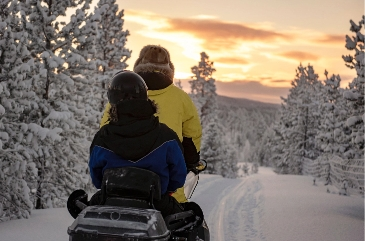 two people sharing a snowmobile at sunset